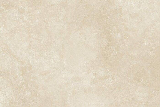 A modern patio enhances outdoor spaces with two wicker chairs and cushions surrounding a small table on a tiled floor. Behind them, sofas are arranged against a brick wall. The gravel path features Brisks Almond Porcelain Paving, providing a slip-resistant surface amidst lush greenery.