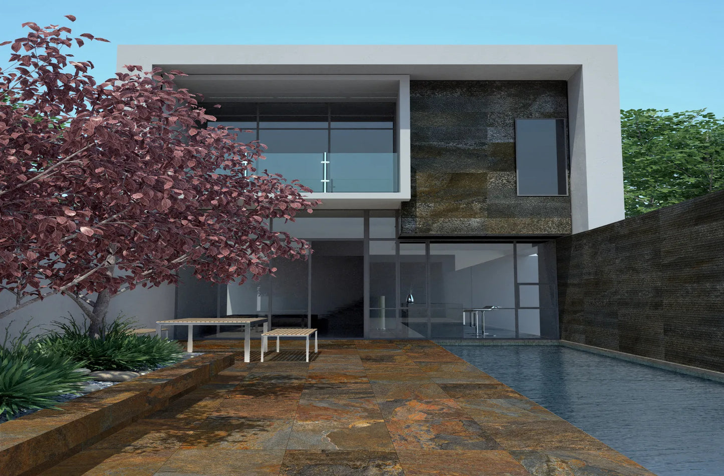 A modern two-story house with a large glass facade showcases a pool extending along a rustic stone patio embellished with slip-resistant Copper Moon Porcelain Paving by Brisks. Outdoor furniture enhances the design, while a tree with reddish leaves offers contrast to the contemporary outdoor areas.