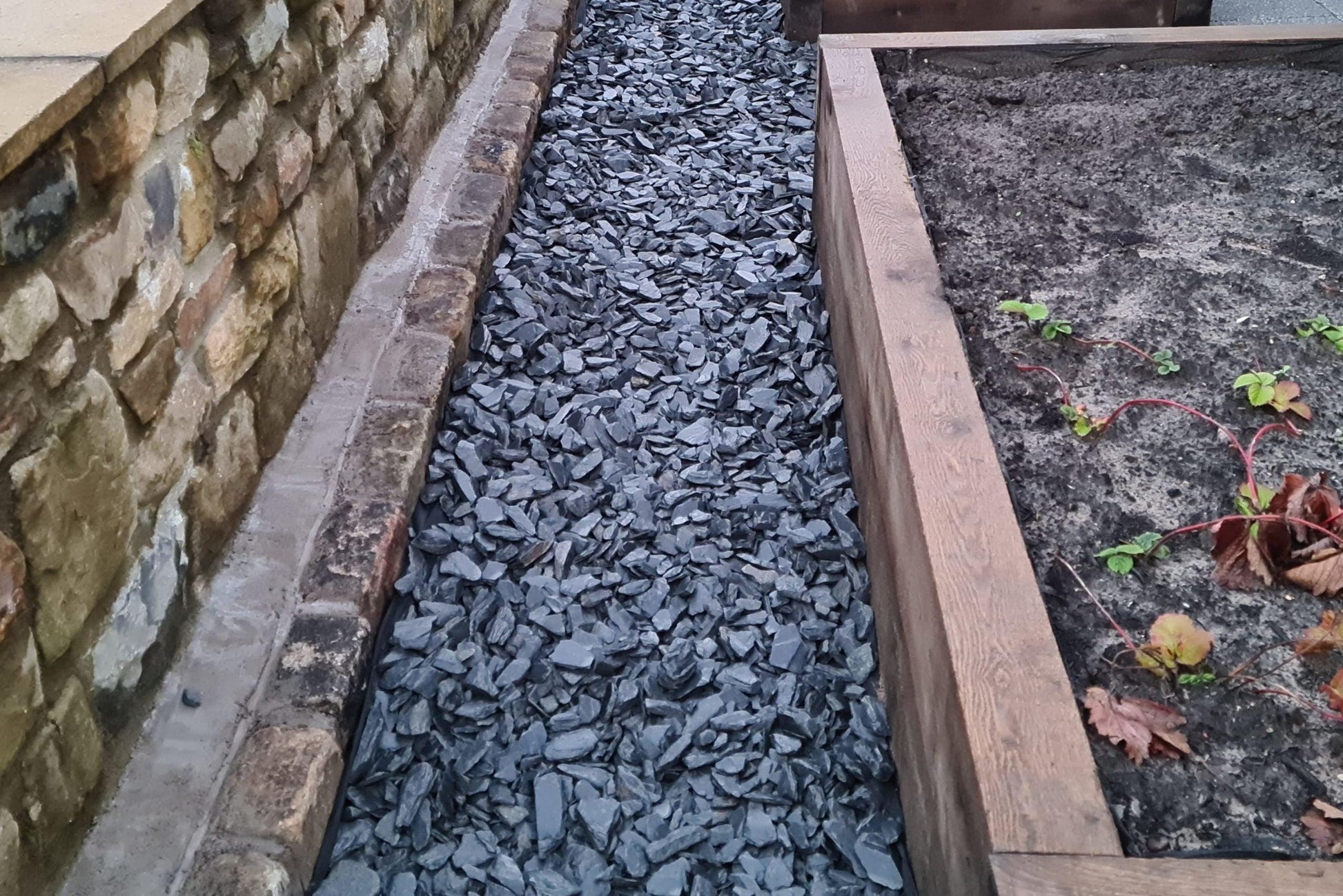a garden area with a stone wall and a wooden planter