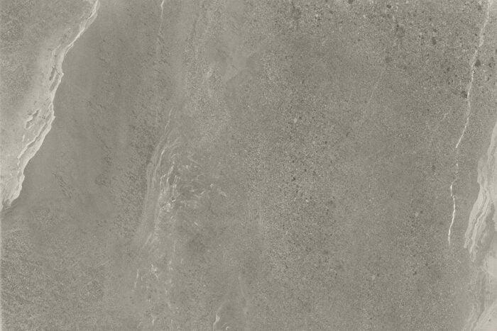 A close-up of a Brisks Britstone Grey Porcelain Paving Slabs surface with subtle variations in texture and color. Faint irregular streaks and marbling patterns give the surface a natural, organic appearance. The uniform grey tone features slight light and dark patches, perfect for a slip-resistant porcelain paving option.