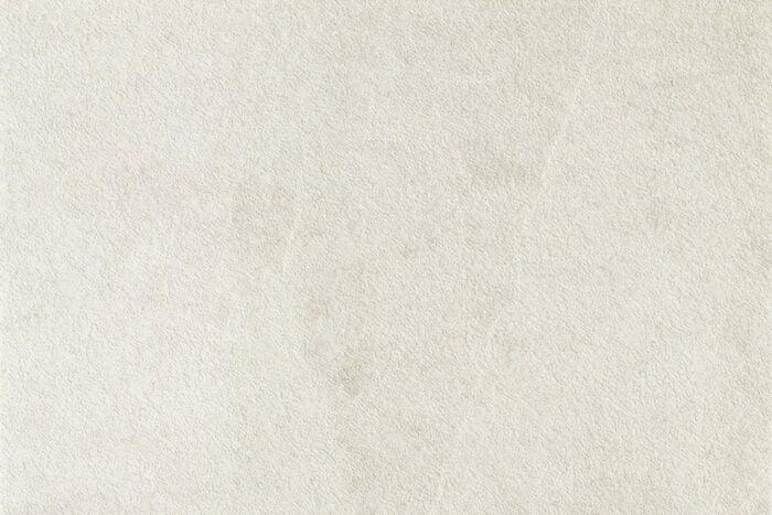 A close-up of a textured, light beige surface with subtle variations in shading, reminiscent of Brisks' Frame Glen Porcelain Paving Slabs. The texture gives the appearance of a soft, slightly rough material.