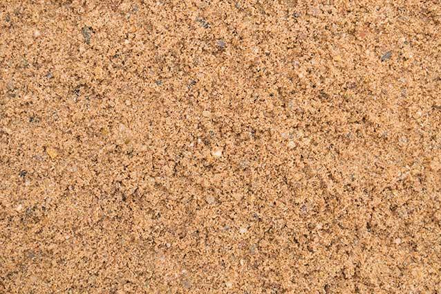 Close-up image of loose, fine Brisks 0-4mm Sharp Sand with a few small pebbles and granules visible. The surface appears dry and granular, showcasing a mixture of light and dark brown particles—perfect for landscaping or block paving projects.