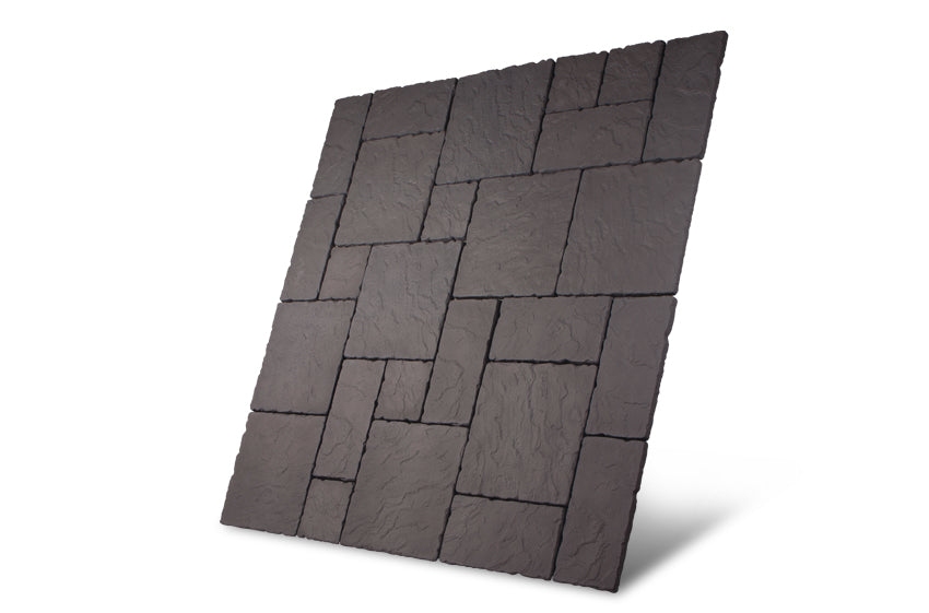 A display of the Welsh Slate Rectory Paving Kit by Bowland Stone from Brisks, featuring interlocking dark gray tiles that exude a rustic allure, arranged in a geometric pattern to create a textured rectangular panel, shown at a slightly tilted angle on a white background.