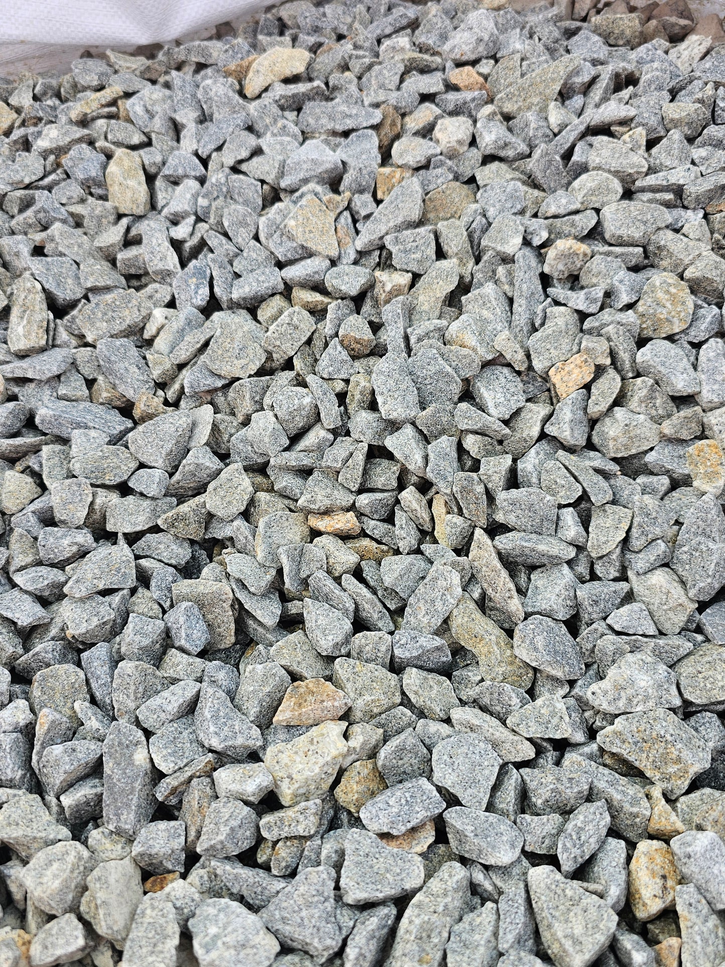 A close-up of a pile of small, rough gray stones or gravel perfect for landscaping. These 20mm Cornish Granite pieces from Brisks vary slightly in size and shape, with hints of beige and brown, making them ideal for enhancing any driveway chippings project.