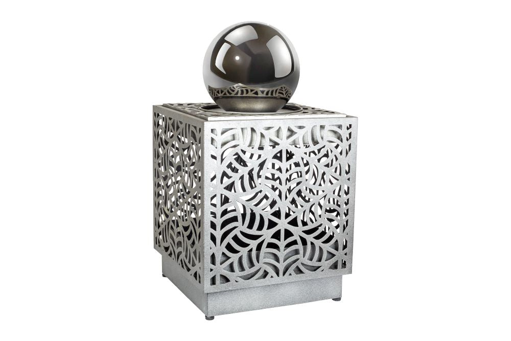 The La Hacienda Rene Cascade Water Feature by La Hacienda is a decorative metallic cube featuring intricate cut-out patterns on all sides, perfect for your outdoor space. Atop the cube rests a reflective, shiny metallic sphere. Its modern and artistic design is further enhanced by an integrated water feature with a subtle recirculating pump.