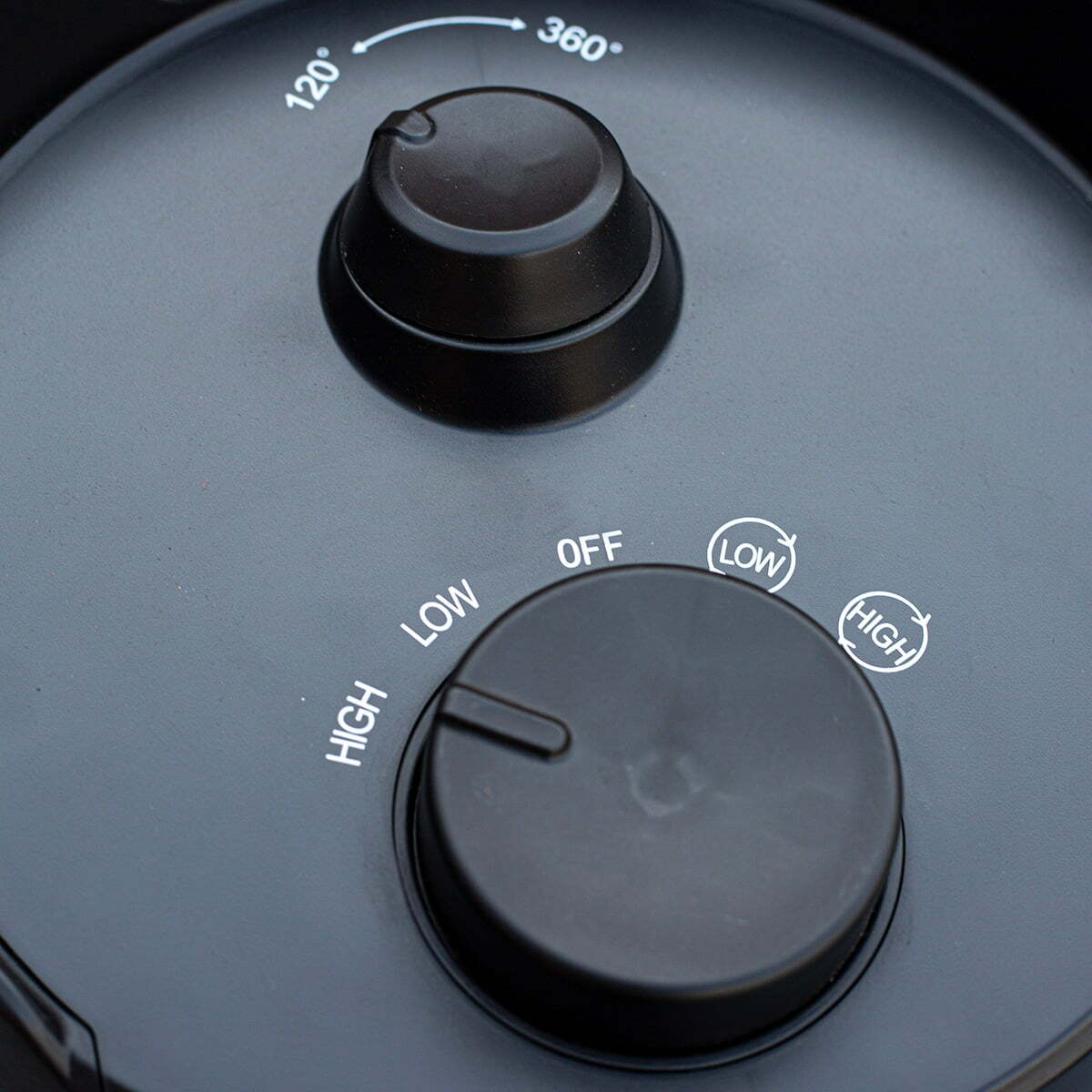 Close-up of the La Hacienda Tabletop Heater's control panel featuring two black dials. The larger dial, adjustable between "OFF," "LOW," and "HIGH," complements the smaller dial displaying angles from 120° to 360°. Both are set to "OFF" against a dark gray panel, ideal for IPX4 outdoor use.