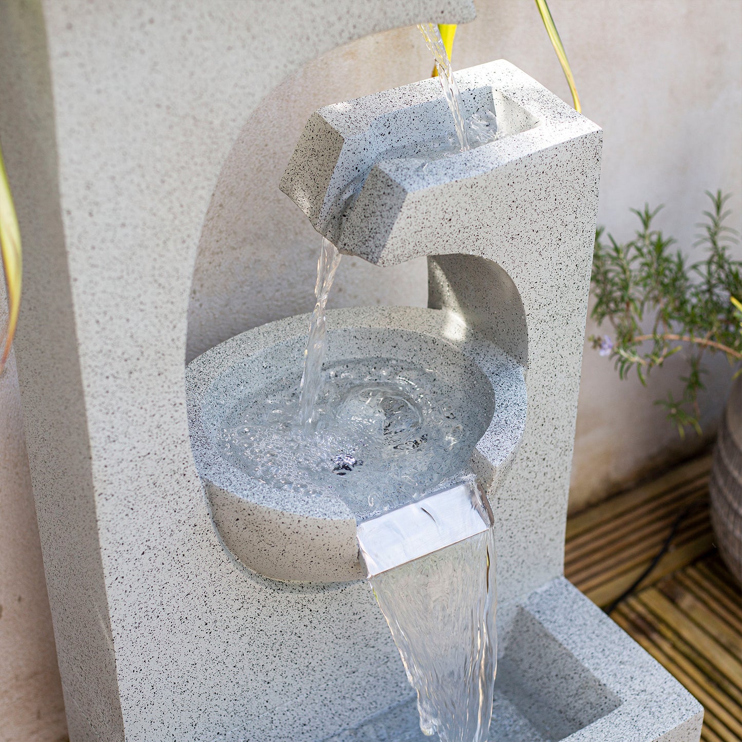 The La Hacienda Ango Falls Water Feature by La Hacienda showcases a contemporary stone design featuring both rectangular and arched elements. Water gracefully cascades from the top basin to the middle and then down to the bottom, beautifully illuminated by LED lights. Made from lightweight poly-resin, this fountain is ideal for gardens with wooden decks and surrounding plants.