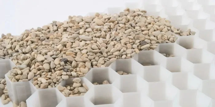 The CORE DRIVE 40-30 / 40-40 Gravel Grid by Core LP features small, light-colored pebbles scattered over a rigid white hexagonal pattern that offers stability and style, making it ideal for eco-friendly landscaping projects with a structured, geometric look.