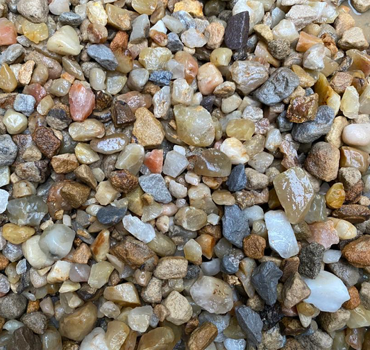 A close-up of Brisks Douglasmuir Quartz shows stones and pebbles in beige, brown, gray, and blue tones scattered on the ground. Perfect for landscaping projects, these stunning stones enhance any space with natural elegance.