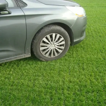 A gray car is parked on an expanse of green grass, its front wheel nestled on a CORE GRASS 40 grid by Core LP. This 800 x 800mm reinforcement effectively ensures proper drainage and preserves the lush landscape while accommodating light commercial traffic.