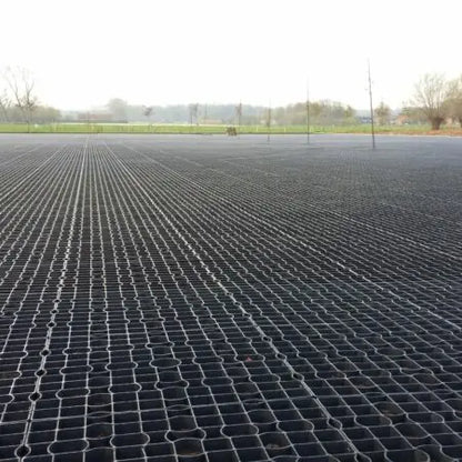 A field features CORE GRASS 40 grass reinforcement grids by Core LP under a cloudy sky. Sparse trees and a grassy area in the distance thrive thanks to the drainage facilitation of the recycled high-density polyethylene (HDPE) mesh structure designed for light commercial traffic.