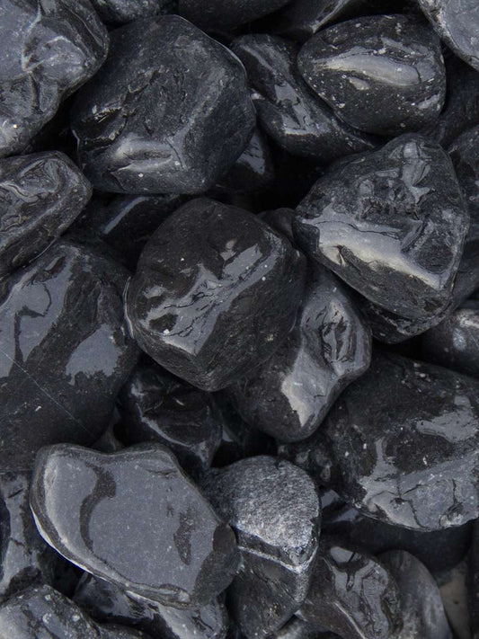 The Brisks 20-40mm Ebony Black Pebbles present a close-up of tightly packed, smooth, glossy stones with reflective surfaces that beautifully catch the light, ideal for adding highlights and a shiny appearance to your garden decor.