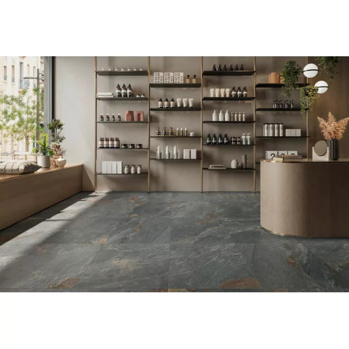 The store's contemporary interior features expansive Frame Gorge Porcelain flooring by Brisks in a sleek grey shade. Shelves are neatly organized with an array of skincare and cosmetic products. A sizable window invites natural light, highlighting plants on the left, while on the right, a round counter is elegantly decorated with dried floral arrangements.