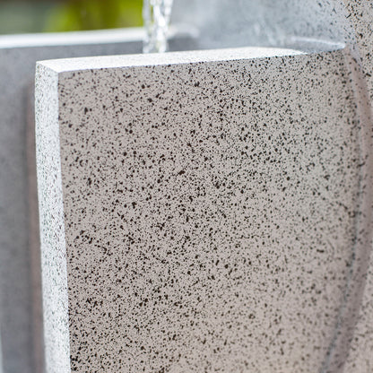 Close-up of a modern, speckled stone water feature with a minimalistic design. Water gently cascades over the edge, creating a soothing and tranquil atmosphere. The granite-like texture adds natural elegance to the scene, enhanced by subtle LED lights that illuminate the La Hacienda Kiso Column Water Feature.