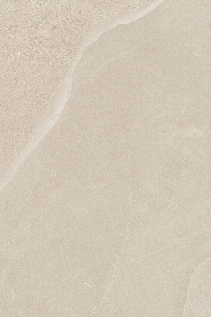 Close-up of a beige stone surface with a textured, slightly rough appearance. The image displays natural color variations and veining, similar to marble or limestone, reflecting the elegant design of Brisks' Kiara Ivory Porcelain Paving.