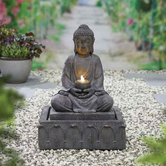 A La Hacienda Water Fountain - Distinctive stands gracefully on a decorative base in a serene garden setting. The fountain features intricate designs and soothing water flow. The surrounding area is adorned with gravel and potted plants, while a blurred garden path fades into the background.