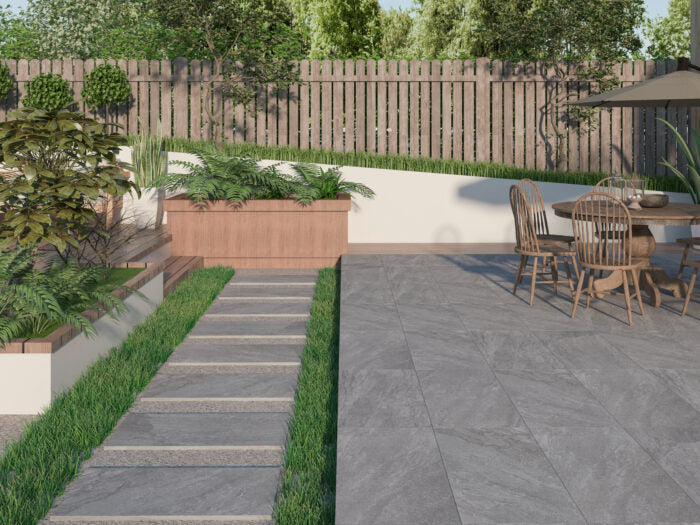 A modern backyard showcases a stone pathway bordered by neatly trimmed grass. On the right, a patio set rests on Brisks' Rasa Grigio Porcelain Paving, known for its premium durability, sheltered by an umbrella. Raised planter boxes filled with greenery line the wooden fence, completing this serene escape.