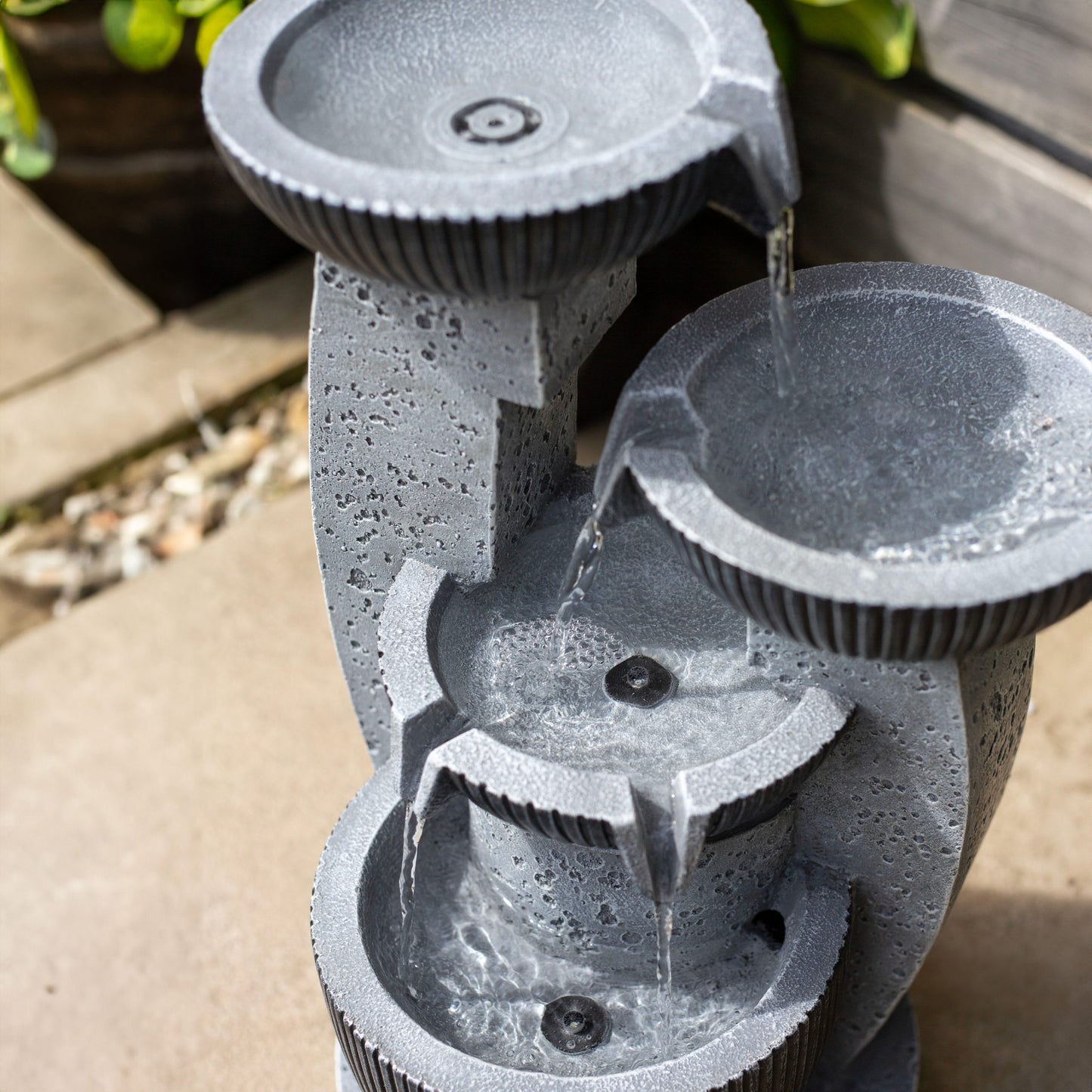 The "Greek Columns incl LEDs" by La Hacienda is a decorative tiered fountain featuring three round basins that elegantly cascade water into one another. Positioned on a patio amid lush greenery, this garden piece beautifully combines natural elegance with the calming sound of flowing water.