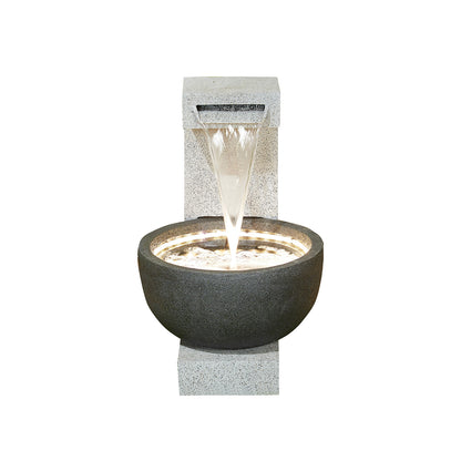 A modern outdoor water fountain featuring a cascading water spout flowing into a round, stone basin, the La Hacienda Solitary Pour (Inc LEDS) Water Feature is illuminated with soft, white LED lights. These lights highlight the gentle stream and make this garden feature from La Hacienda a decorative focal point.