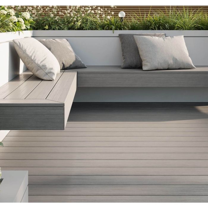 A modern patio with Deck&Grass Woodgrain Composite Decking and built-in seating featuring gray cushions. The low-maintenance space is bordered by white planters filled with greenery, creating a serene outdoor area.