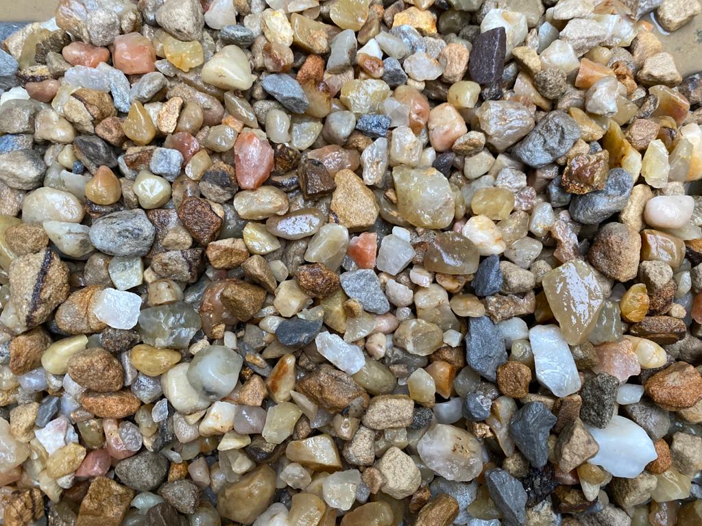 A close-up of variously colored smooth pebbles and small stones, from brown to gray and beige, some slightly wet. Douglasmuir Quartz by Brisks adds elegance. The image captures diverse textures and natural patterns perfect for landscaping projects.