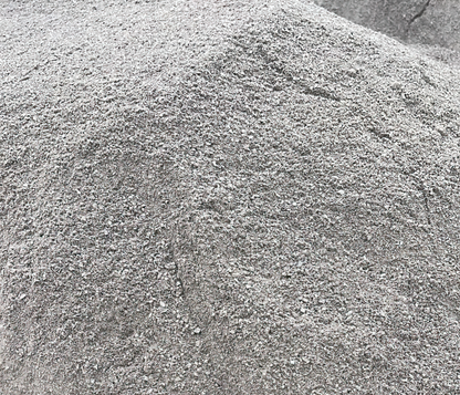 A large mound of fine gray Grano Dust by Brisks is clustered together, forming uneven peaks and slopes. The gravel, commonly used as a sub-base layer, consists of small, coarse particles of varying shades of gray, giving a textured, slightly rough appearance.