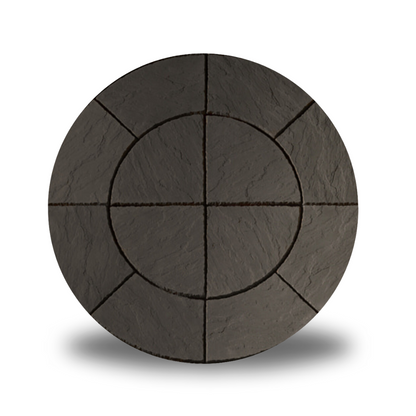 A circular stone patio design with a concentric circle pattern and radiating segments, resembling a sunburst. Made from the Welsh Slate Chalice Circle by Bowland Stone, the dark gray stones have a textured surface. The image features a soft shadow underneath, suggesting it is slightly elevated—a stunning addition to garden features by Brisks.