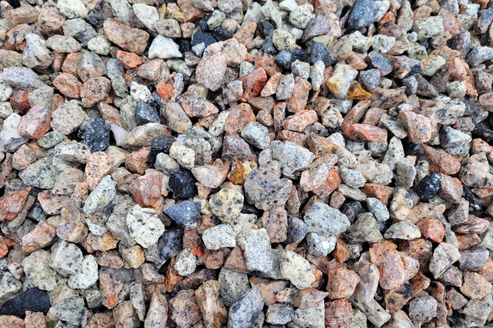 Close-up view of a pile of small, irregularly-shaped landscaping gravel stones in various shades of gray, white, orange, and black. The stones have a rough texture and are unevenly distributed — perfect for driveways or garden paths featuring 14-20mm Silver Grey Granite Chippings by Brisks.