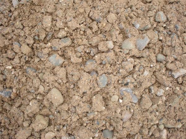 A close-up view of a mixture of sandy soil and small rocks, ideal for construction applications. The color is predominantly light brown with various Brisks 20mm All In Ballast Aggregate stones scattered throughout. The rough and uneven texture suggests suitability for concrete projects.