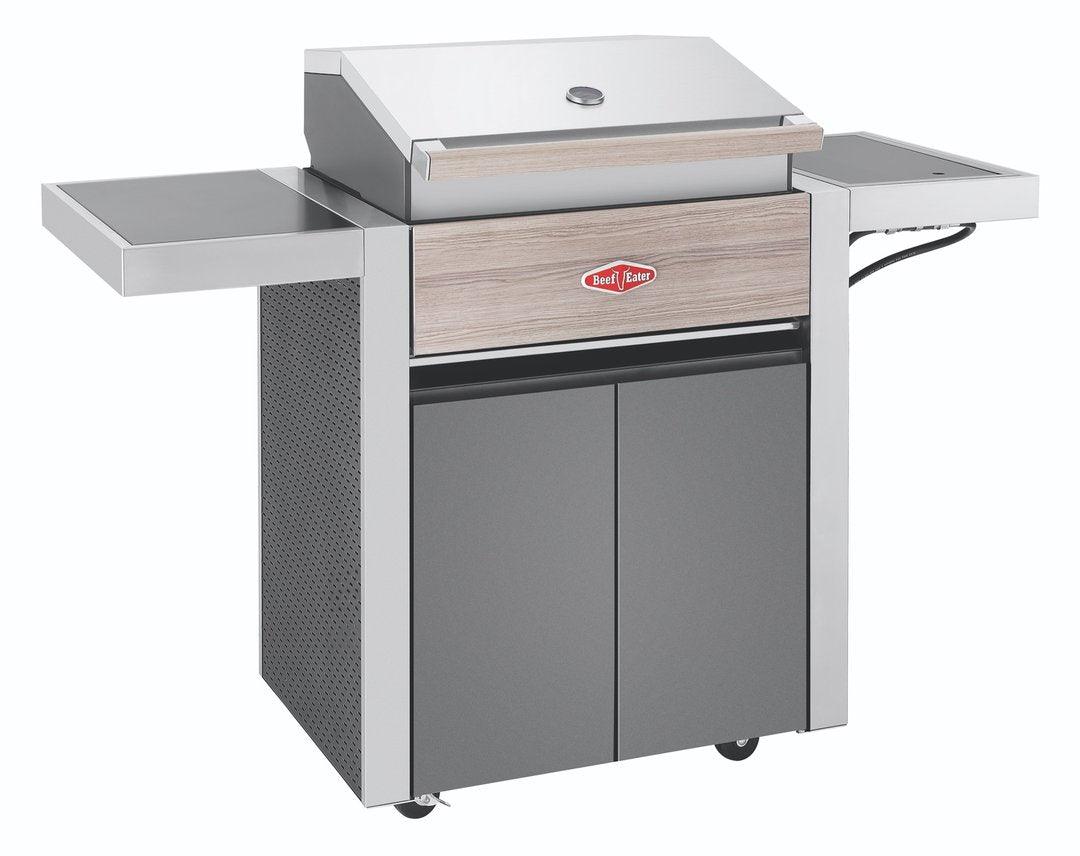 A modern, stainless steel BeefEater 1500 Series 3 Burner BBQ & Trolley with a closed lid. The grill features a wooden accent on the front, two side shelves, a lower cabinet with double doors, and a red insignia with white text on the front. The Brisks BeefEater 1500 Series 3 Burner BBQ & Trolley is on four wheels for easy mobility and enhances any outdoor cooking experience.