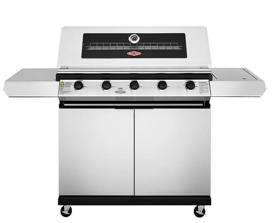 Introducing the Brisks BeefEater 1200S Series 5 Burner BBQ & Trolley, a top-of-the-line BBQ with a large stainless steel main cooking area. It features a thermometer on the lid, five control knobs, two side shelves for convenience, and a cabinet below for storage. Perfect for Outdoor Living with its caster wheels ensuring easy mobility.