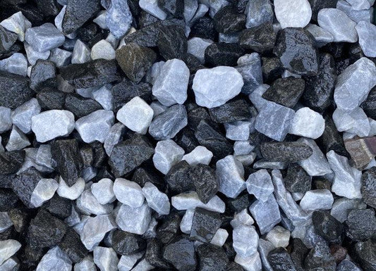 A close-up view of a pile of 20mm Polar Black Ice Chippings by Brisks in various shapes and sizes. The stones are primarily black and white, creating a contrasting pattern. The texture of these decorative garden chippings appears rough and uneven.