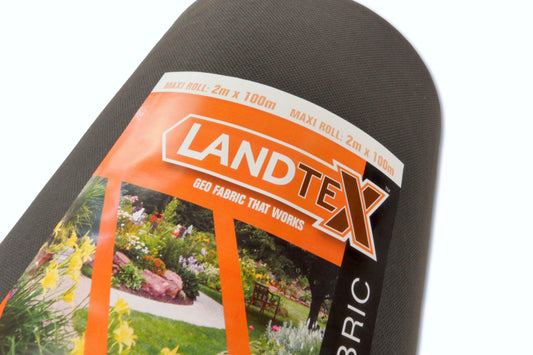 Close-up of a Brisks LANDTEX Weed Membrane Fabric roll. The label, featuring the Brisks LANDTEX Weed Membrane Fabric logo in bold orange and white text, indicates the roll size as 2m x 100m. The background shows landscaped gardens with flowers and greenery, showcasing this eco-friendly weed barrier's effective weed control capabilities.