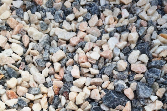An assortment of small, irregularly-shaped gravel stones, varying in color from light beige, gray, to dark charcoal, fills the frame. The stones are closely packed, creating a textured and rugged surface perfect for garden landscaping with Brisks 20mm Polar Pink Marble Chippings adding a pop of color.