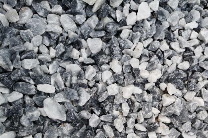 An image showing a close-up view of a pile of small, mixed gravel stones in shades of white and gray. The stones are irregular in shape and size, creating a textured and rough surface, ideal for garden landscaping with their Brisks 20mm Polar Blue Marble Chippings adding a touch of elegance.