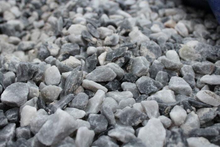 A close-up photo of a mixture of small gray and white gravel stones, including some 20mm Polar Blue Marble Chippings from Brisks, creating a textured and uneven surface. The stones vary in size and shape, with colors ranging from light to dark shades of gray, white, and soft blue—ideal for elegant garden landscaping.
