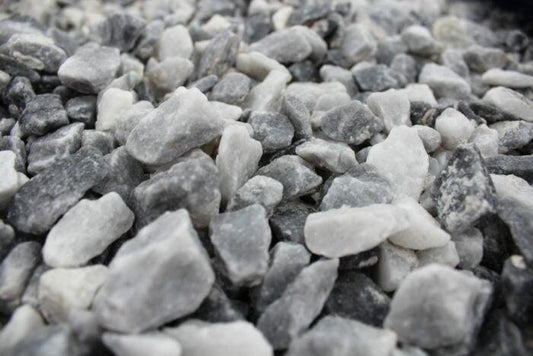 A close-up image showcasing a collection of small, roughly broken Brisks 20mm Polar Blue Marble Chippings in shades of gray and white. The stones vary in size and shape, adding a textured and uneven appearance to the garden landscaping surface.