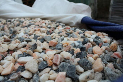 Close-up view of a pile of mixed color gravel stones, ranging in shades of white, pink, and gray. Among them are Brisks 20mm Polar Pink Marble Chippings, perfect for garden landscaping. A white and blue fabric partially covers the chippings in the background.
