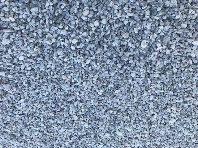 A close-up view of a large collection of small, Brisks 20mm Polar Blue Marble Chippings, spread out to cover the entire frame. The stones are irregularly shaped and vary slightly in size, creating a textured surface perfect for garden landscaping.