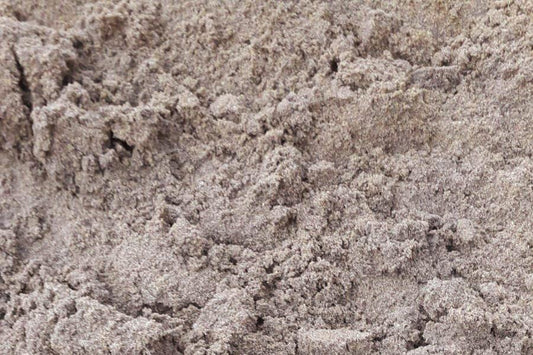 A close-up image of a rough, uneven sandy surface with varying textures and shades of beige and gray, resembling the appearance of dry, compacted Brisks Plastering Sand.