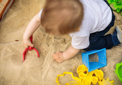 a toddler playing in the sand with toys