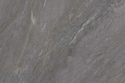 A close-up of a slab of gray stone with natural texture and veining. The Charcoal Grey colour surface displays various shades of gray with patches of lighter and darker streaks running across it, creating an abstract and rugged appearance, ideal for outdoor durability in Brisks Ultra Aspen Anthracite Porcelain Paving Tiles.