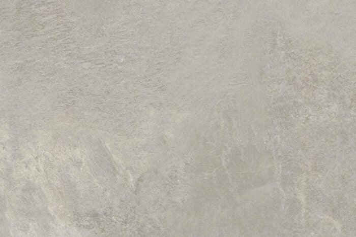 A close-up image of a textured stone surface with subtle variations in gray tones. The stone appears natural, with minor imperfections and slight veins adding to its realistic appearance. Brisks' Ultra Aspen Grigio Porcelain Paving Tiles showcase a durable finish, ranging from light to medium gray.
