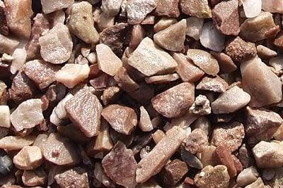 A close-up image of variously shaped and sized brown and beige pebbles, ideal for landscaping. The stones are irregularly shaped with a range of textures, giving a rough and natural appearance. The densely packed Brisks 20mm Staffordshire Pink Gravel covers the entire frame of the image.