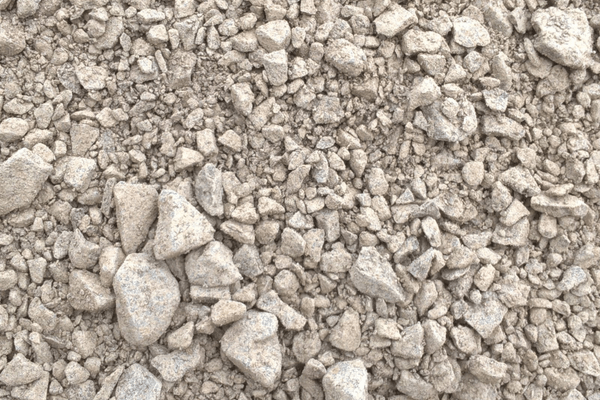 A close-up view of a Brisks MOT Type 1 Frost Resistant gravel surface, featuring various sizes of light gray rocks and pebbles, ranging from small grains to larger stones. The texture appears rough and uneven, creating a natural, rugged look that is both durable and frost-resistant.