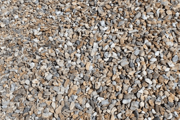 A close-up view of a large pile of small, irregularly shaped pebbles and stones in varying shades of beige, gray, and white. This Brisks 10-20mm Shingle Gravel boasts a rough texture with stones closely packed together, filling the entire frame—perfect for landscaping or drainage projects.