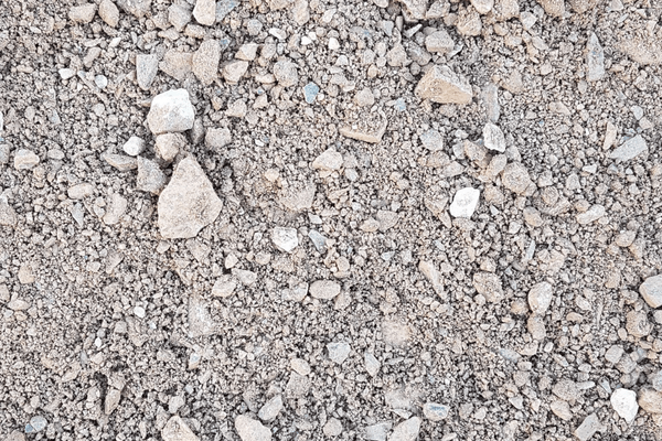 Close-up image of a dry, rocky ground surface composed of **Brisks MOT Type 1 Frost Resistant** sub-base material, featuring small pebbles, stones, and fine gravel. The texture is uneven and dusty, with various shades of gray and brown.