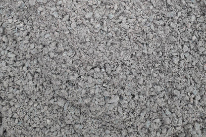 A close-up image of a pile of crushed gray Grano Dust by Brisks, often used as a sub-base layer. The Grano Dust pieces vary in size and shape, giving the surface a rough, uneven texture.