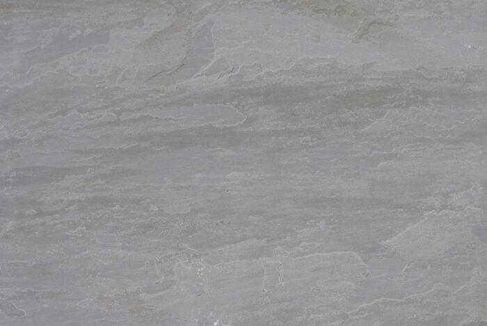 A close-up of a Brisks Kandla Grey Sandstone Paving Slabs surface, showcasing its natural texture with subtle variations in color and faint, wavy striations.