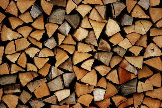 Stacks of cut firewood, showing the circular cross-sections of Kiln Dried Birch Firewood from Brisks along with their bark. The premium quality firewood is neatly arranged in a repeating pattern, creating a textured and natural background.
